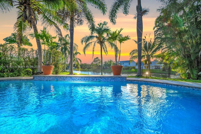 pool at dusk with an outdoor pool and fence