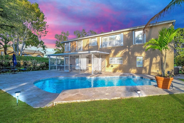 back of house at dusk featuring a patio, stucco siding, central AC unit, a sunroom, and an outdoor pool