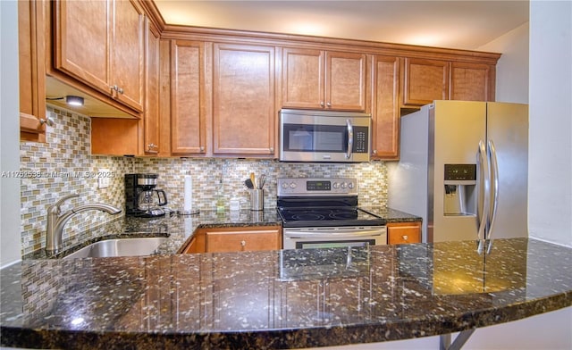 kitchen with brown cabinets, stainless steel appliances, decorative backsplash, a sink, and dark stone counters