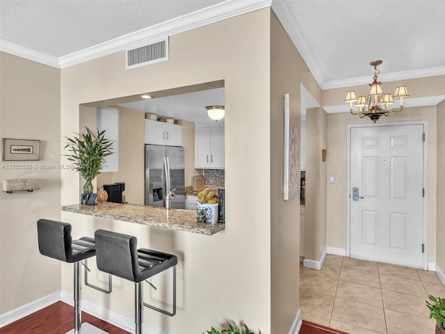 kitchen with ornamental molding, white cabinets, visible vents, and stainless steel refrigerator with ice dispenser