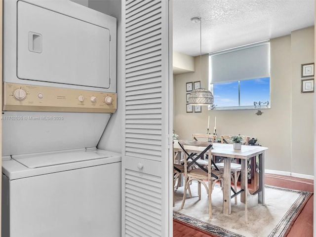 clothes washing area with laundry area, baseboards, stacked washer and clothes dryer, wood finished floors, and a textured ceiling