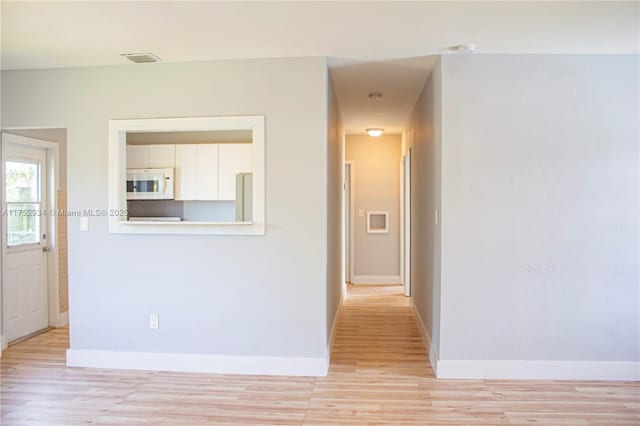 hallway with light wood-style flooring, visible vents, and baseboards