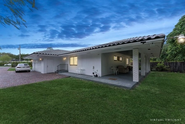 back of house with a tiled roof, stucco siding, fence, and a lawn
