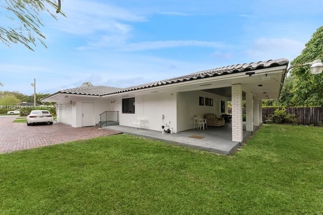 rear view of property with fence, stucco siding, a tile roof, a lawn, and a patio area