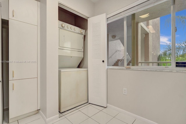 laundry area featuring laundry area, light tile patterned floors, baseboards, and stacked washer and clothes dryer