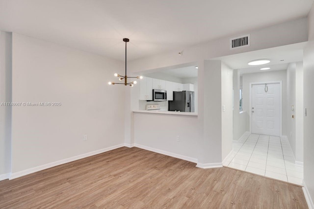 spare room with an inviting chandelier, light wood-style flooring, visible vents, and baseboards