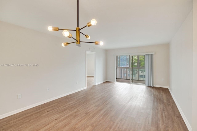 spare room with a notable chandelier, baseboards, and wood finished floors