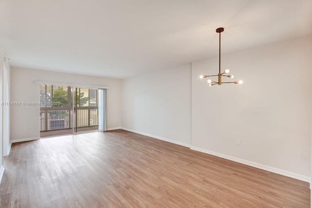 empty room with light wood finished floors, baseboards, and a notable chandelier