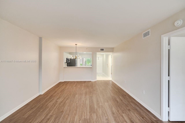 empty room featuring a notable chandelier, baseboards, visible vents, and wood finished floors