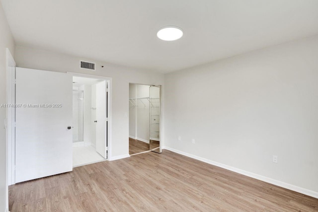 unfurnished bedroom featuring a walk in closet, visible vents, light wood-style flooring, and baseboards