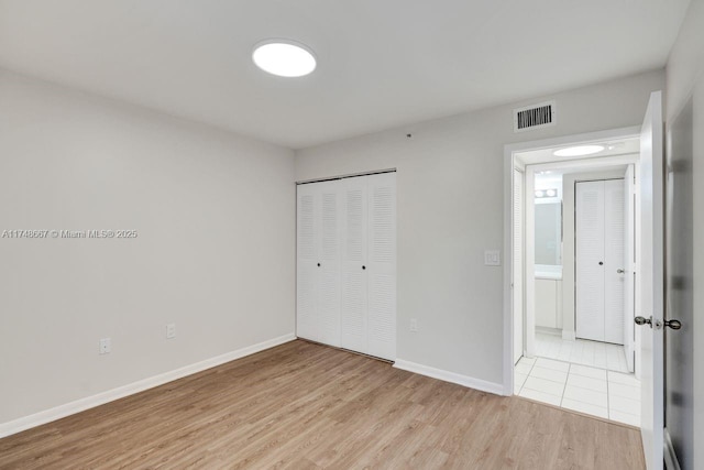 unfurnished bedroom featuring light wood-style flooring, a closet, visible vents, and baseboards