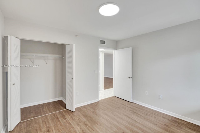 unfurnished bedroom featuring a closet, visible vents, baseboards, and wood finished floors