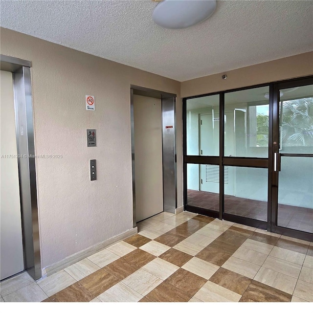 spare room with elevator, baseboards, a textured wall, and a textured ceiling