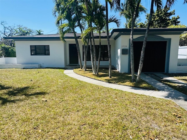 view of front of property with a front yard, fence, driveway, stucco siding, and a garage