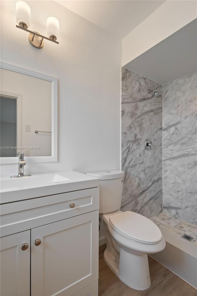 bathroom with toilet, a tile shower, wood finished floors, and vanity