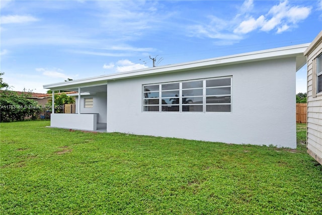 rear view of property featuring a yard, fence, and stucco siding