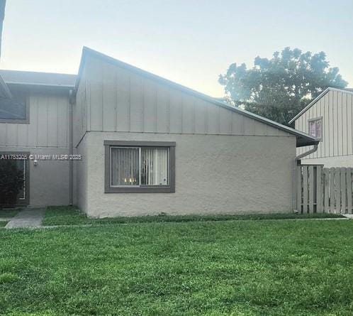 view of side of home with stucco siding, a yard, and fence