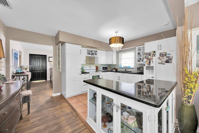 kitchen with dark countertops, white appliances, visible vents, and glass insert cabinets