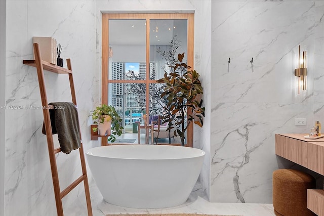 bathroom featuring marble finish floor, stone wall, a freestanding tub, and vanity