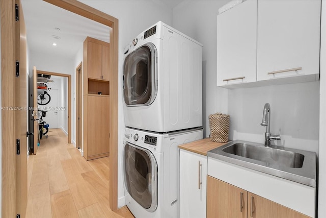 laundry room featuring light wood-type flooring, cabinet space, stacked washing maching and dryer, and a sink