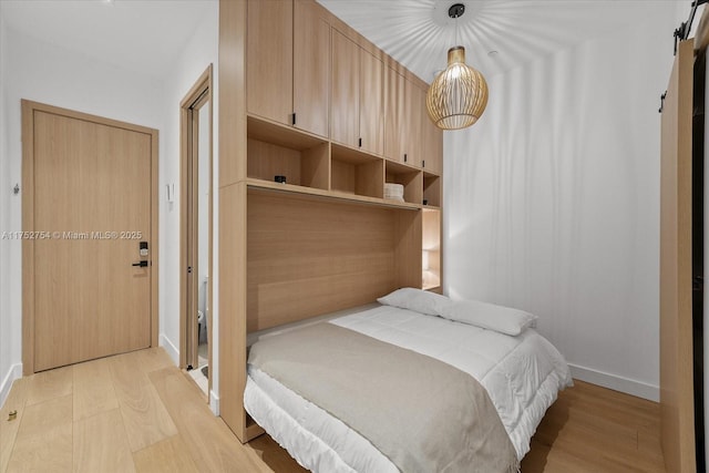 bedroom with a barn door, light wood-type flooring, and baseboards