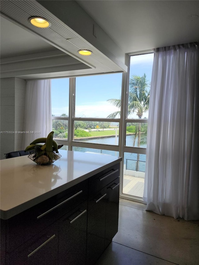 kitchen featuring light countertops, a water view, finished concrete floors, a kitchen island, and dark cabinets