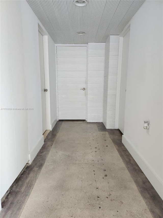 hall featuring concrete flooring and baseboards