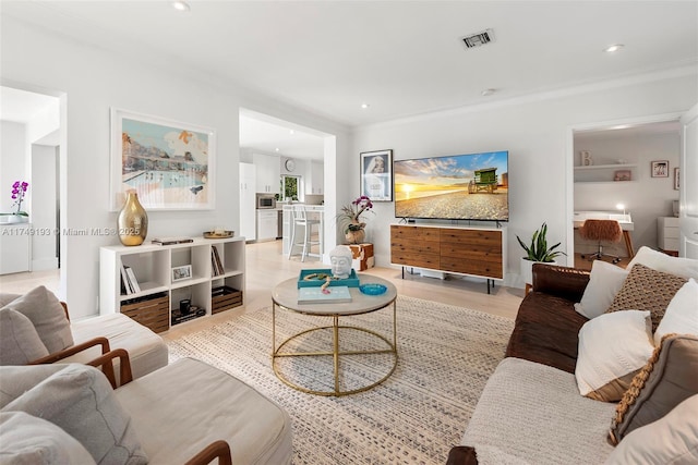 living room featuring ornamental molding, light wood-style flooring, visible vents, and recessed lighting