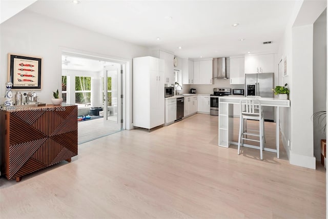 kitchen with wall chimney exhaust hood, stainless steel appliances, light wood-type flooring, white cabinetry, and a sink