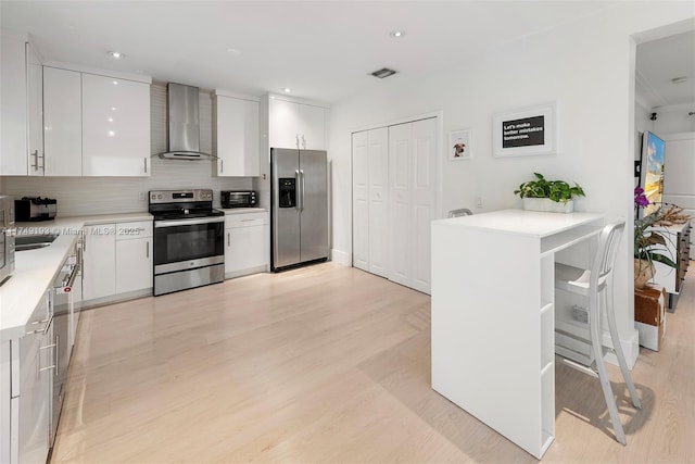 kitchen featuring stainless steel appliances, wall chimney exhaust hood, light wood-style flooring, and white cabinets