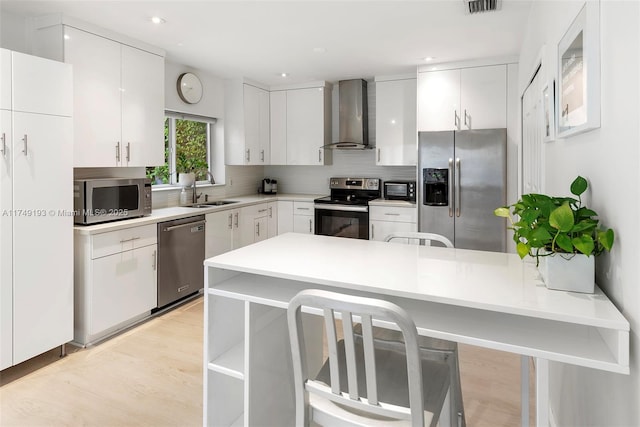 kitchen featuring stainless steel appliances, tasteful backsplash, a sink, wall chimney range hood, and a peninsula