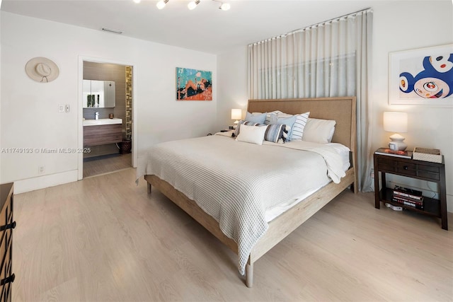 bedroom featuring ensuite bathroom, light wood finished floors, and visible vents