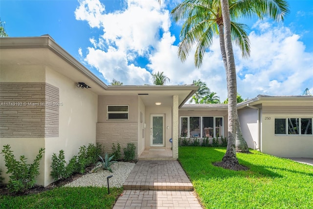 view of exterior entry featuring brick siding, a lawn, and stucco siding