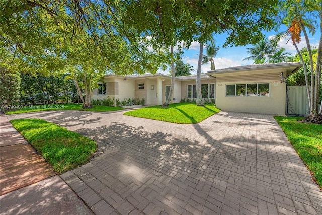 ranch-style home with decorative driveway, fence, a front lawn, and stucco siding