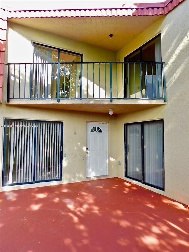 exterior space featuring a balcony, a tile roof, a patio, and stucco siding