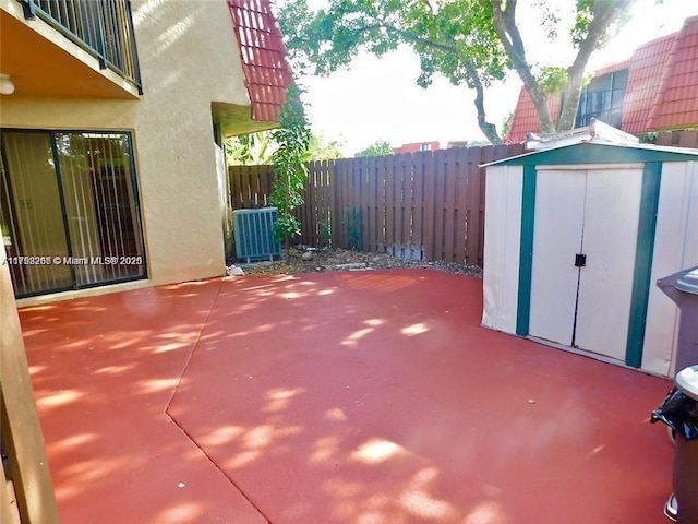 view of patio featuring an outbuilding, a storage shed, cooling unit, and fence