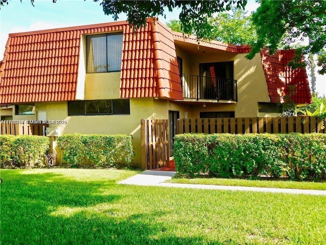 view of front of home featuring a tile roof, mansard roof, stucco siding, a balcony, and a front lawn