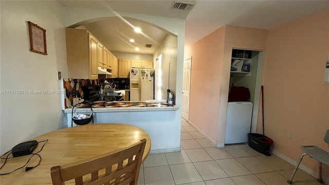 kitchen with white refrigerator with ice dispenser, visible vents, tile counters, arched walkways, and fridge