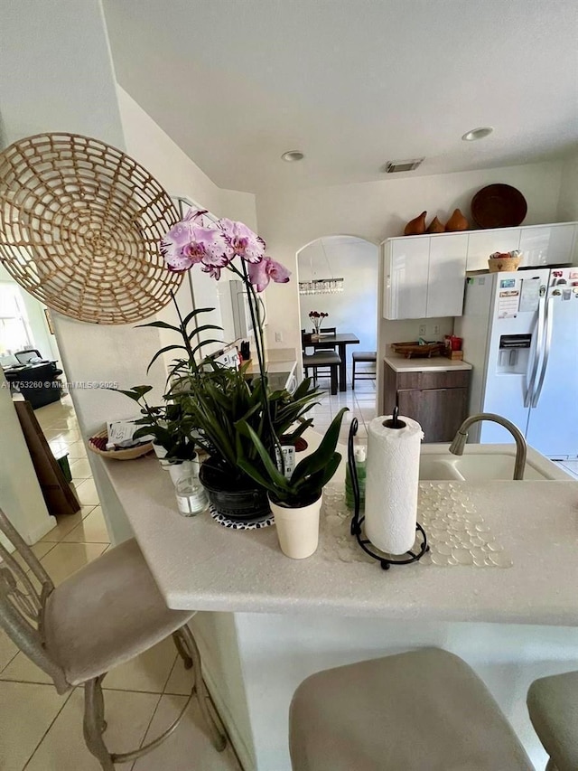 kitchen featuring visible vents, white cabinets, light countertops, white fridge with ice dispenser, and light tile patterned flooring