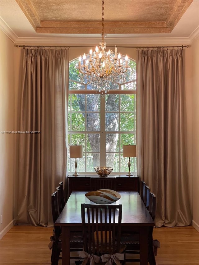 dining area with ornamental molding, a tray ceiling, and light wood finished floors