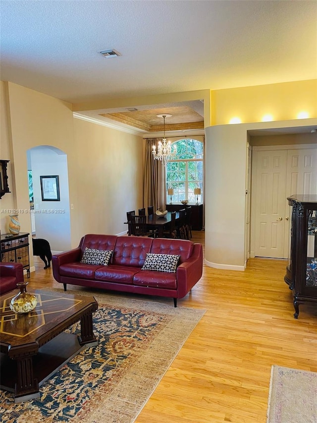 living area with arched walkways, a tray ceiling, visible vents, an inviting chandelier, and light wood-style floors