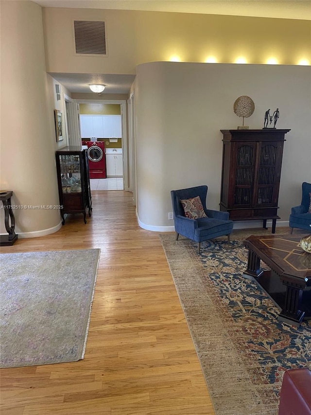 hallway with light wood-type flooring, washer and dryer, visible vents, and baseboards