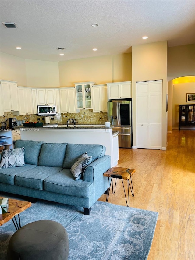 living room with visible vents, arched walkways, a textured ceiling, light wood-type flooring, and recessed lighting