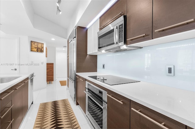 kitchen featuring light tile patterned floors, a sink, dark brown cabinets, appliances with stainless steel finishes, and light countertops