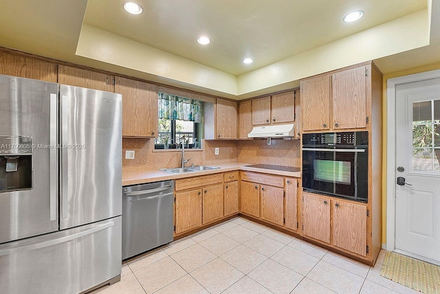 kitchen featuring light countertops, light tile patterned flooring, a sink, under cabinet range hood, and black appliances