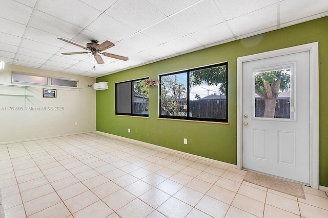 spare room featuring a ceiling fan, an AC wall unit, a drop ceiling, and light tile patterned flooring