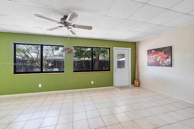 unfurnished room with ceiling fan, a drop ceiling, and baseboards