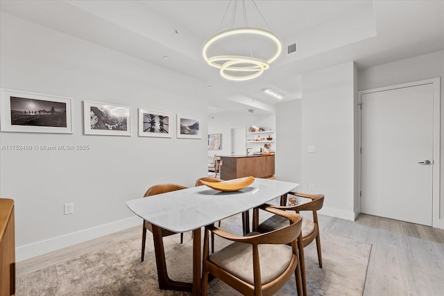 dining space featuring light wood-style flooring, baseboards, a raised ceiling, and a chandelier