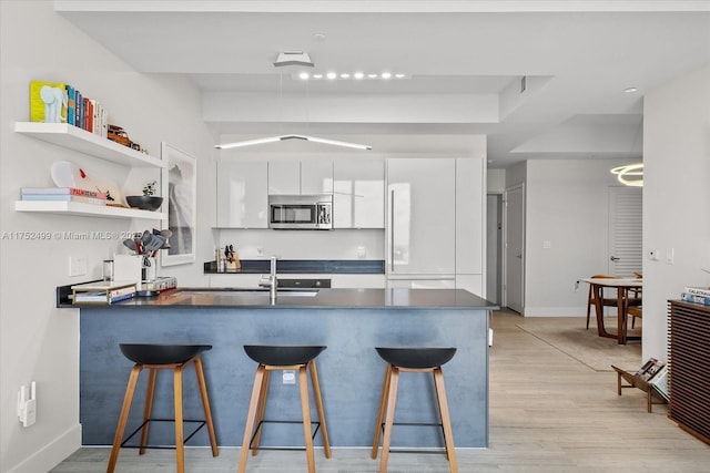 kitchen with white cabinets, dark countertops, modern cabinets, stainless steel microwave, and a peninsula