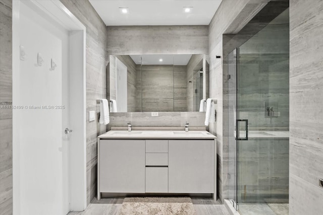 full bath featuring a sink, double vanity, a shower stall, and tile walls